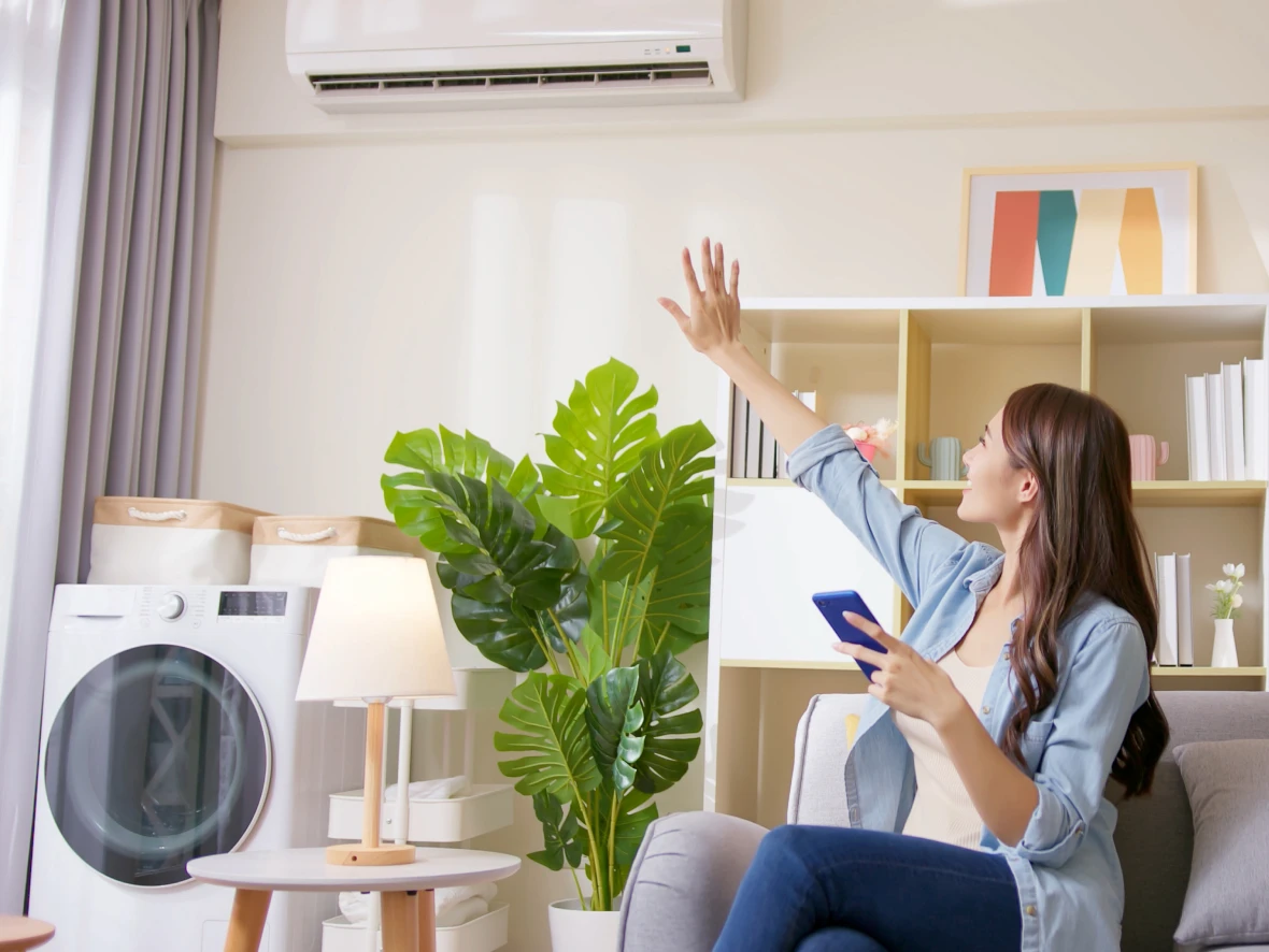 Woman adjusting air conditioner with remote control.