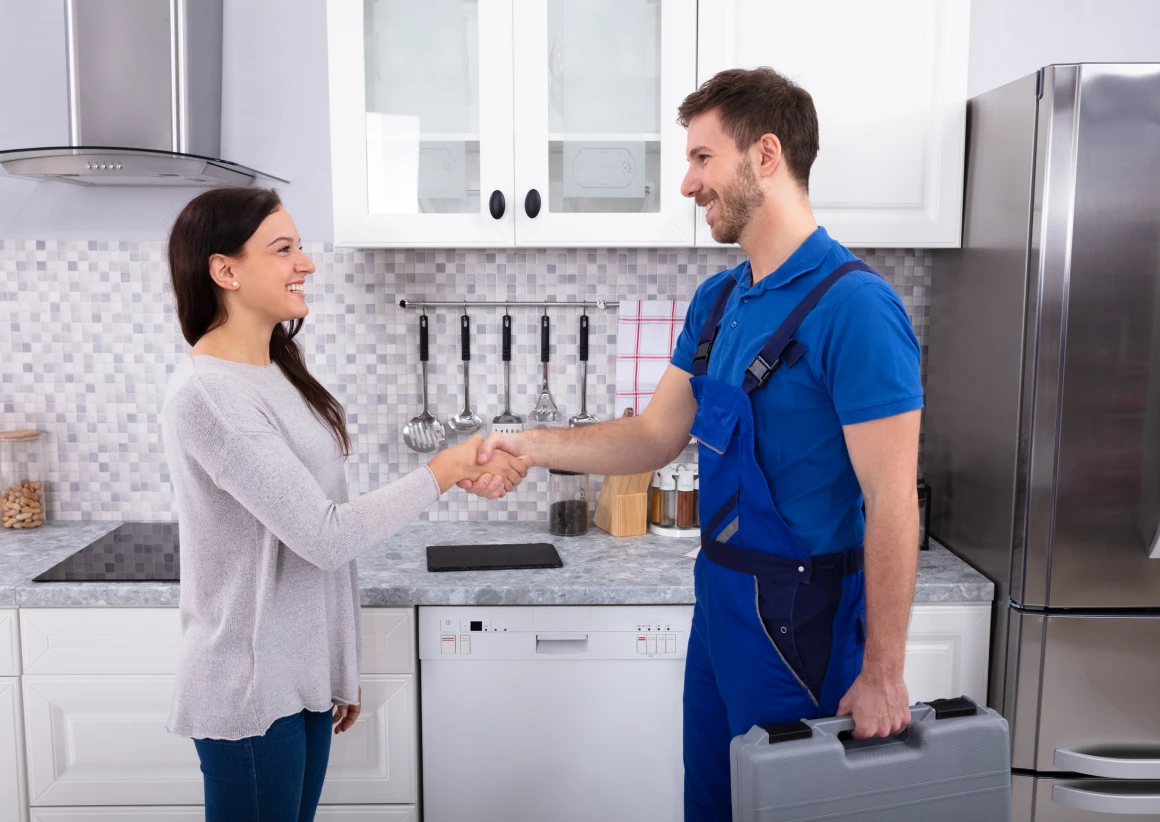 Woman shaking hands with repairman in kitchen.